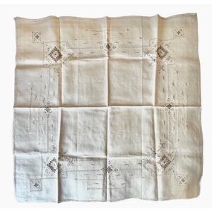 May include: Cream-colored linen square tablecloth with embroidered floral and geometric patterns. The embroidery is in a muted gray color, with detailed corner designs and linear accents. The cloth is folded, showing the texture and design details.