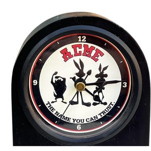 May include: Black and white clock with a white face and black hands. The clock face features the words "ACME" in red letters and the phrase "The name you can trust." in black letters. The clock face also features a silhouette of Bugs Bunny, Wile E. Coyote, and Road Runner.