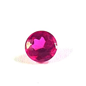 Puede incluir: Una gema redonda, facetada, de color magenta intenso con un corte brillante. La gema se encuentra sobre un fondo blanco, mostrando su color vibrante y claridad. Adecuada para la fabricación de joyas.