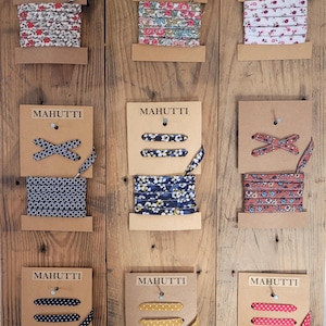 Peut inclure: Neuf bobines de ruban avec différents motifs floraux et à pois. Chaque bobine est étiquetée "MA HUTTI" et comporte un échantillon de ruban noué en un nœud.