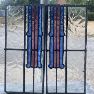 May include: Two rectangular stained glass panels featuring a central vertical design with blue and pink glass segments. The panels are framed in black lead cames and include textured, clear glass panes on the outer sides of the central columns.
