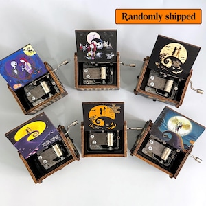 K&ouml;nnte beinhalten: Eine Sammlung von Holz-Spieluhren mit verschiedenen Illustrationen aus "The Nightmare Before Christmas". Jede Box hat eine Kurbel und einen Klappdeckel mit farbenfrohen Kunstwerken. Der Text "Randomly shipped" ist sichtbar.