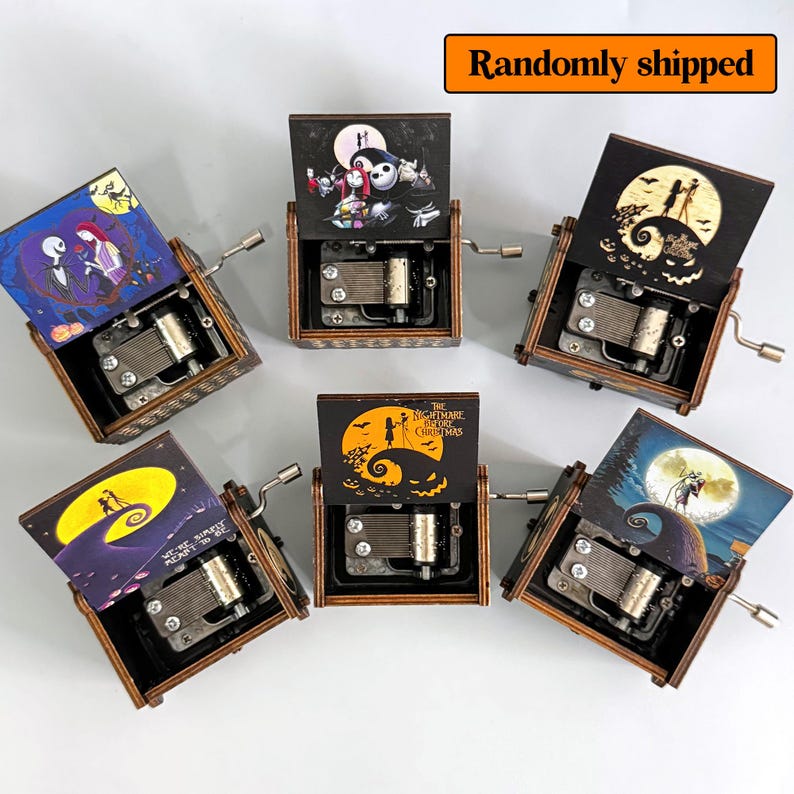 K&ouml;nnte beinhalten: Eine Sammlung von Holz-Spieluhren mit verschiedenen Illustrationen aus "The Nightmare Before Christmas". Jede Box hat eine Kurbel und einen Klappdeckel mit farbenfrohen Kunstwerken. Der Text "Randomly shipped" ist sichtbar.