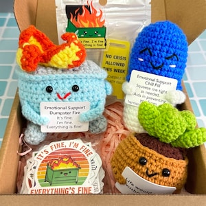 Puede incluir: Una caja de regalo contiene varios artículos de ganchillo. Hay un contenedor de basura azul claro con una llama, una pastilla azul y una maceta marrón con una planta verde. Cada artículo tiene un pequeño letrero con texto. También se incluyen pegatinas con un incendio en un contenedor de basura.