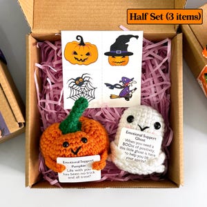 K&ouml;nnte beinhalten: Ein Halloween-Geschenkset in einem Karton. Das Set enth&auml;lt einen geh&auml;kelten orangefarbenen K&uuml;rbis und einen wei&szlig;en Geist, beide mit Karten. Ebenfalls enthalten sind vier tempor&auml;re Tattoos mit Halloween-Designs.