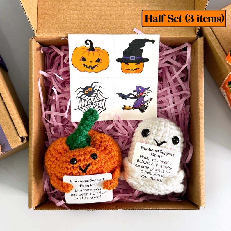K&ouml;nnte beinhalten: Ein Halloween-Geschenkset in einem Karton. Das Set enth&auml;lt einen geh&auml;kelten orangefarbenen K&uuml;rbis und einen wei&szlig;en Geist, beide mit Karten. Ebenfalls enthalten sind vier tempor&auml;re Tattoos mit Halloween-Designs.