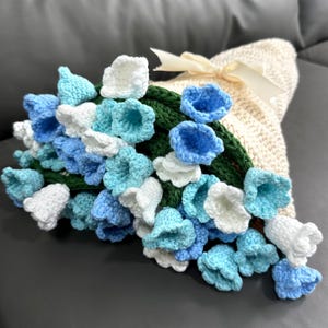 May include: A crocheted bouquet of blue, white, and green flowers in a cream-colored crocheted basket.