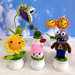 Puede incluir: Una colección de personajes de plantas y zombies de crochet del popular videojuego Plants vs. Zombies. Los personajes se muestran en macetas blancas con musgo verde. Los personajes incluyen un girasol, una trampa para moscas de Venus, un zombie, un hongo y dos girasoles.