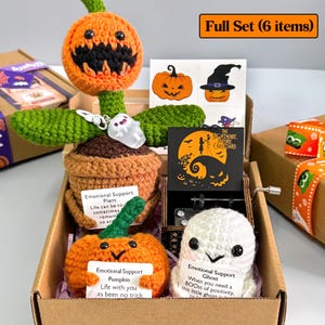 K&ouml;nnte beinhalten: Ein Halloween-Geschenkset mit einer geh&auml;kelten K&uuml;rbispflanze, Aufklebern, einer Spieluhr und einem geh&auml;kelten Geist, pr&auml;sentiert in einem Karton. Der Text "Full Set (6 items)" ist sichtbar. Das Set enth&auml;lt den Text "Emotional Support".