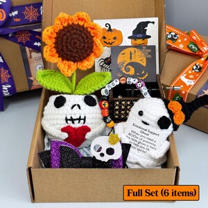 May include: A Halloween-themed gift set in a cardboard box. Includes a crocheted skull planter with a sunflower, a ghost, a skull-shaped ornament, a bracelet, and decorative cards. The set is decorated with orange, purple, and black accents.