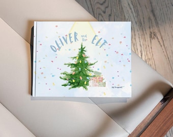 Könnte beinhalten: Ein Buch mit dem Titel "Oliver und der Elf" mit einer Aquarell-Illustration eines Weihnachtsbaums mit Geschenken darunter. Der Buchumschlag ist hellblau mit weißen Konfetti.