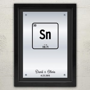 May include: A framed silver metal print with a black and white periodic table element graphic for tin, Sn, atomic number 50, atomic weight 118.71. The print has the text "David & Olivia 4.23.2015" at the bottom.