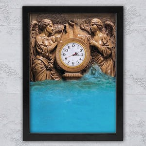 Könnte beinhalten: Eine gerahmte Wanduhr mit einem detaillierten Relief von zwei Engelsfiguren, die ein goldfarbenes Zifferblatt flankieren. Das Zifferblatt hat schwarze Ziffern und Zeiger. Der untere Teil des Kunstwerks zeigt eine blaue Wasserszene.