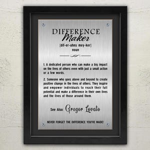 May include: A framed silver plaque with the word "DIFFERENCE Maker" in bold, black font. The plaque includes a definition, pronunciation, and the phrase "Never Forget The Difference You've Made!" The frame is black.