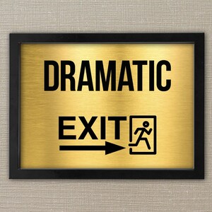 May include: A black framed sign with a gold background. The sign reads "Dramatic Exit" with a black silhouette of a person running to the right.