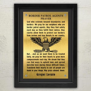 May include: A gold plaque with a black frame, featuring a prayer for border patrol agents. The plaque includes a stylised eagle with outstretched wings and the text "Border Patrol Agents Prayer". The prayer reads: "God who extends beyond boundaries and borders- We pray for our neighbours who are border patrol agents. May they find safety each day as they fulfil their duties. May clarity allow them to protect our borders from serious and true threats to our country. But... Just as we want them to be treated fairly, we pray for their hearts to grow more compassionate each day. We dream that they can find ways to uphold laws and spread merciful love during these difficult times. Transform their hearts to see all people are made in your image. May grace abound. Amen." The plaque is signed "Gregor Lovato".