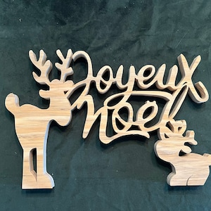 Może przedstawiać: Drewniana ozdoba choinkowa z dwoma sylwetkami reniferów i tekstem "Joyeux Noel" w ozdobnym kroju pisma.