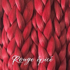 May include: Close-up of a woven material in a vibrant red hue. The texture is created by interwoven strands, forming a braided pattern. The words "Rouge épicé" are written in white script across the bottom.
