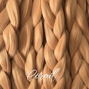Può includere: Primo piano di un motivo intrecciato in tonalità marrone chiaro e beige. La trama ricorda una grande treccia o un tessuto intrecciato. La parola "Corail" è scritta in corsivo nella parte inferiore dell'immagine.