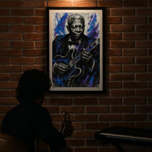 May include: A framed portrait of B.B. King playing a guitar hangs on a brick wall. The artwork features a blue and purple color palette. A person is seen in the foreground playing a guitar, with a keyboard in the background.