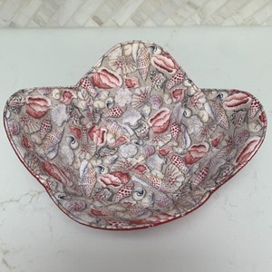 Puede incluir: Un bol de tela rojo y blanco con un patrón de conchas marinas. El bol tiene forma de estrella y un borde festoneado.