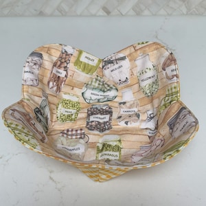 May include: A yellow and white gingham fabric bowl with a print of jars filled with various vegetables and fruits. The jars are labeled with the names of the contents, such as "Pickles", "Peas", "Cherries", "Carrots", "Asparagus", "Yellow AI", "Wild Leek", "Garlic", "Red", "Chili", "Dill", and "Darlk".