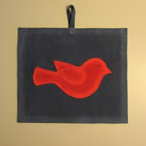 May include: A red felt bird applique on a dark blue felt background. The bird is attached to a loop of fabric for hanging.