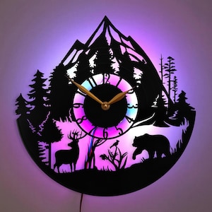 May include: A black vinyl record clock with a mountain, trees, deer, and bear silhouette design. The clock face has gold hands and a colorful LED light behind it.