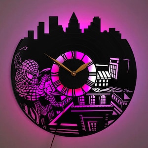 Pode incluir: Relógio de disco de vinil preto com silhueta de cidade e design do Homem-Aranha. O relógio tem um mostrador iluminado em rosa e branco com ponteiros dourados. Um item decorativo único.