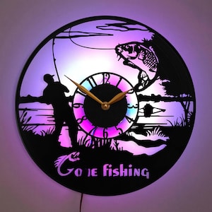 May include: A black vinyl record clock featuring a silhouette of a person fishing and a fish leaping from the water. The clock face has a rainbow coloured background with gold hands and black numbers. The text "Gone Fishing" is printed below the clock face.