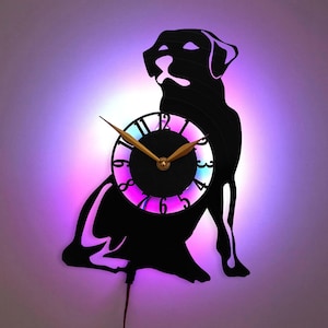 May include: A black silhouette of a Labrador Retriever dog with a clock face in the center. The clock face has a black background with white Roman numeral hour markers and gold hands. The clock is illuminated with a multi-colored LED light.