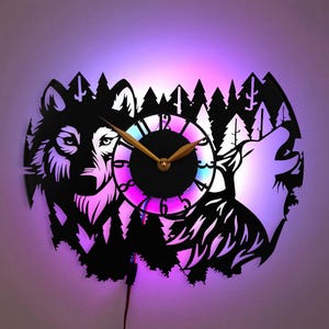 May include: A black vinyl record clock with a wolf silhouette and a forest scene. The clock face is a circle with gold hands and a colorful LED light ring. The clock is lit with a purple and pink glow.