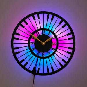 May include: A circular wall clock featuring a black frame designed like piano keys radiating outward. The center has a black dial with black numbers and gold-colored hands. The clock is illuminated by a vibrant purple and blue LED light glow.