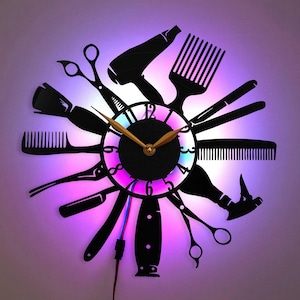 Puede incluir: Reloj de pared negro con temática de peluquería, con siluetas de tijeras, peines, un secador de pelo y otras herramientas de estilismo. El reloj tiene una luz brillante multicolor alrededor de la esfera y manecillas doradas.