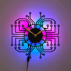 Puede incluir: Un reloj de pared con un diseño de placa de circuito negro, una esfera circular central y manecillas doradas. El reloj está iluminado desde atrás por luces LED vibrantes que cambian entre tonos de azul, morado y rosa.