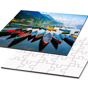 May include: A jigsaw puzzle featuring a scenic image of colorful boats on a lake with mountains in the background. The puzzle is partially assembled, with the completed image on top and the unassembled pieces below.