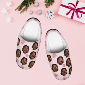 Peut inclure: Une paire de pantoufles roses avec un motif répété d'un visage de femme et d'une fleur rose. Les pantoufles ont un intérieur blanc et un extérieur rose. Le fond est rose clair avec des décorations de fête.