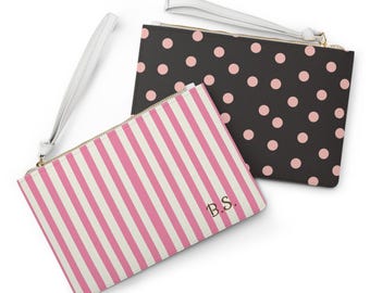 May include: Two zippered clutches. One is black with pink polka dots, the other has pink and white vertical stripes. Both have a white wrist strap and gold-colored zipper. The striped clutch has the initials "B.S." printed on it.
