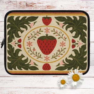 Puede incluir: Una funda para portátil con un diseño de estilo vintage que presenta una fresa roja grande rodeada de hojas verdes y flores rosas. El fondo es de color crema con un borde amarillo.