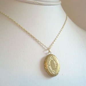 May include: A gold-toned oval locket necklace with a delicate chain. The locket has an ornate design with a raised center.