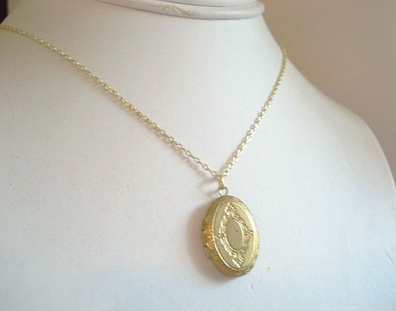 May include: A gold-toned oval locket necklace with a delicate chain. The locket has an ornate design with a raised center.