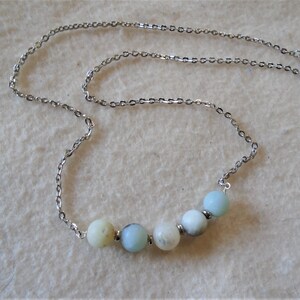 Puede incluir: Un collar de cadena de plata con una fila de seis cuentas redondas de color azul claro y blanco.