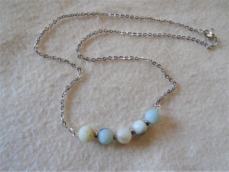 Puede incluir: Un collar de cadena de plata con una fila de seis cuentas redondas de color azul claro y blanco.