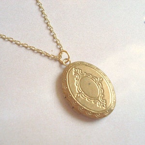 May include: A gold chain necklace with a gold oval locket pendant. The locket has a detailed, ornate design.