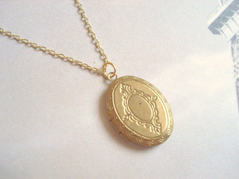 May include: A gold chain necklace with a gold oval locket pendant. The locket has a detailed, ornate design.
