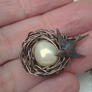 May include: A delicate silver wire nest pendant with a white pearl and a bronze bird charm.