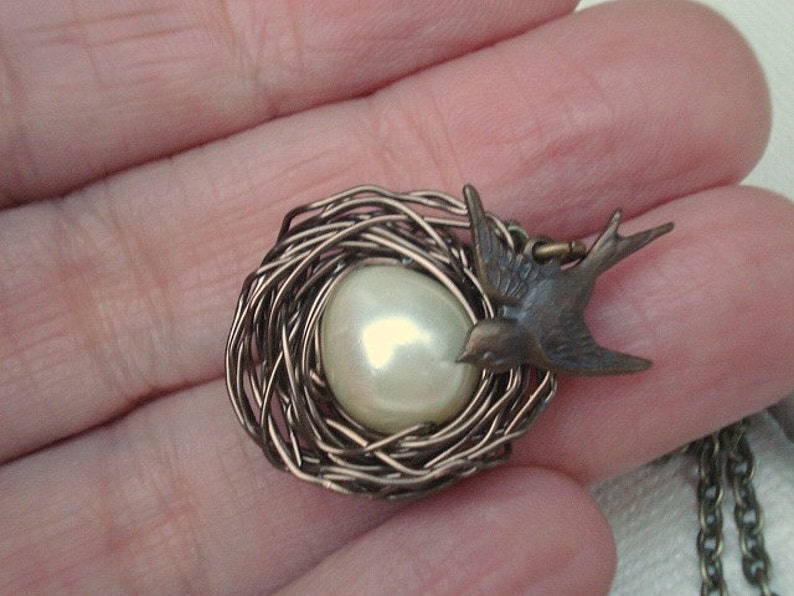 May include: A delicate silver wire nest pendant with a white pearl and a bronze bird charm.