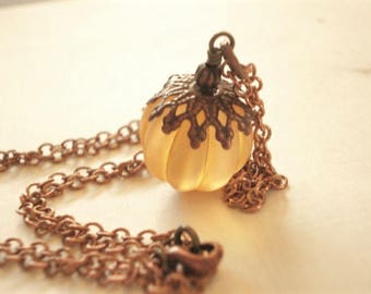 May include: A vintage-style necklace featuring a pumpkin-shaped pendant. The pendant is a soft yellow color with a decorative bronze-colored filigree cap. The necklace chain is also bronze-colored, creating a cohesive, antique aesthetic.