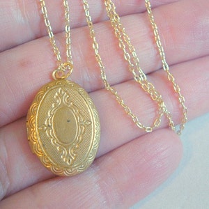 May include: A gold-tone locket necklace with a detailed oval pendant. The chain is a delicate, thin chain.