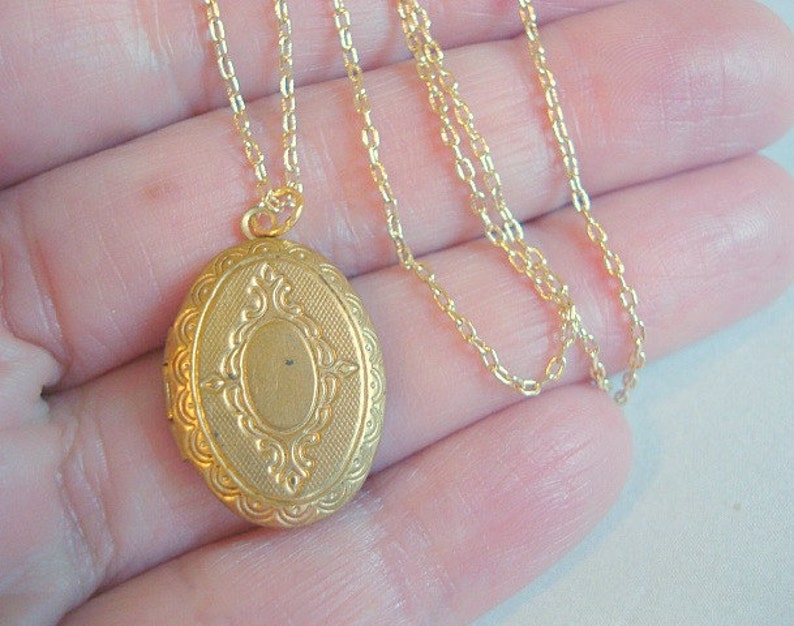 May include: A gold-tone locket necklace with a detailed oval pendant. The chain is a delicate, thin chain.